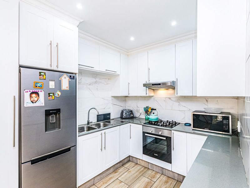 Modern kitchen featuring white cabinetry, stone countertops, marble-look tile backsplash, built-in oven, gas hob, and wood-look tile flooring.