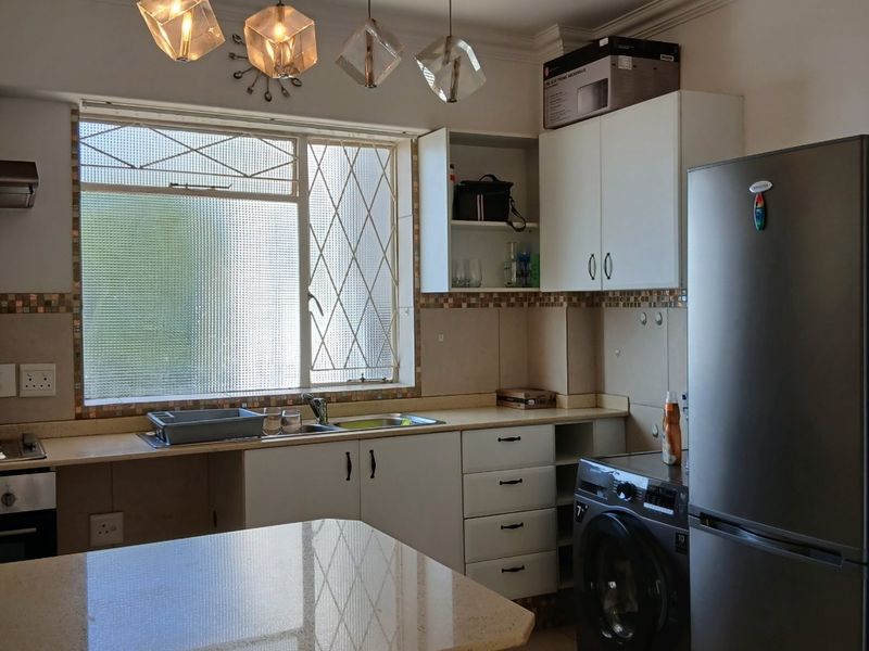A functional kitchen featuring stone countertops, tiled backsplash, built-in cabinetry, and a breakfast bar, illuminated by modern pendant lighting.