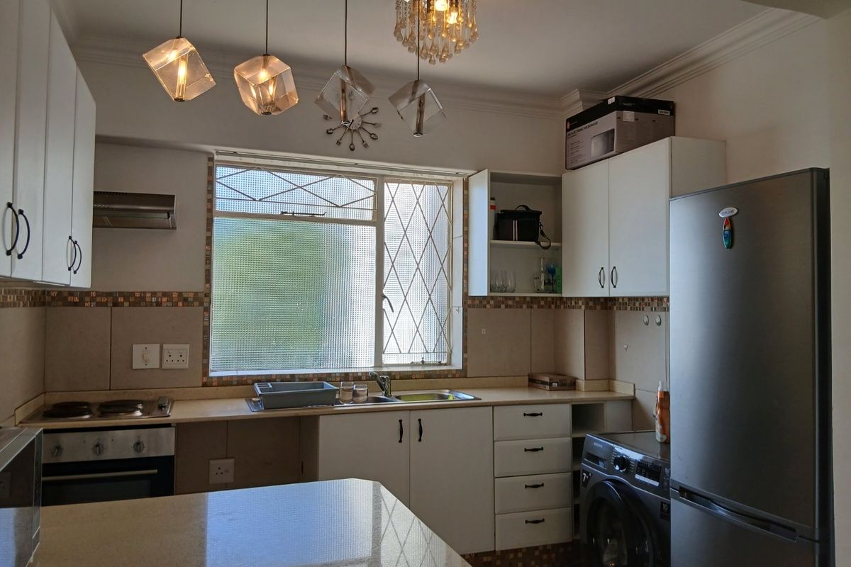 A functional kitchen featuring white cabinetry, stone countertops, a built-in oven and hob, and a window with security bars.