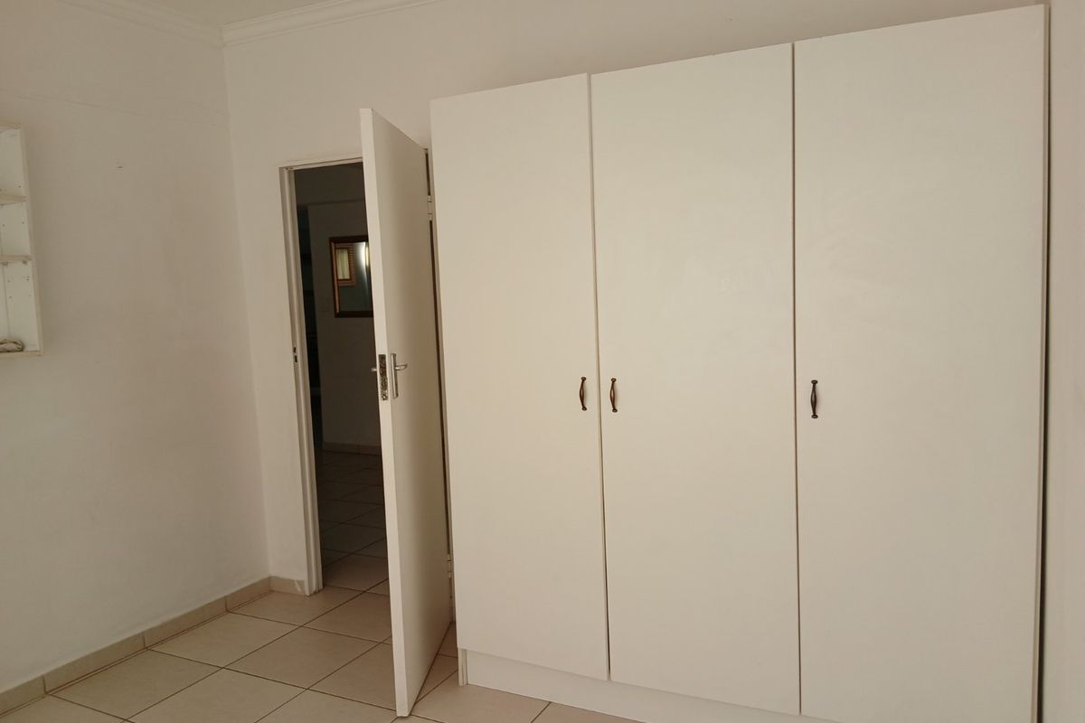 A clean, empty bedroom featuring neutral tiled flooring and white built-in cupboards, offering a blank canvas for personalization.