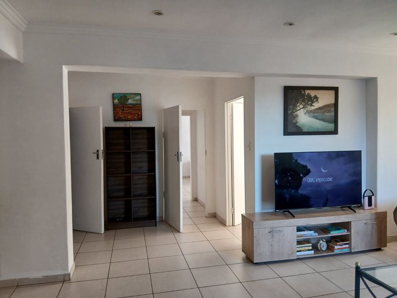 A living room area featuring neutral tiled flooring, recessed downlighting, and multiple internal doorways leading to other parts of the apartment.