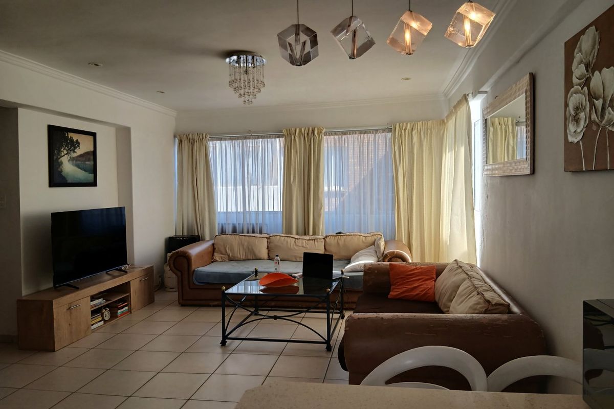 A spacious living room featuring tiled flooring, decorative pendant lighting, and cove molding, offering a comfortable and well-lit area for relaxation.