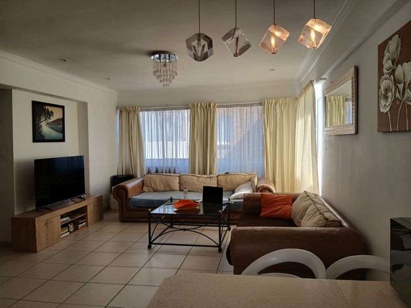 A spacious living room featuring tiled flooring, decorative pendant lighting, and cove molding, offering a comfortable and well-lit area for relaxation.