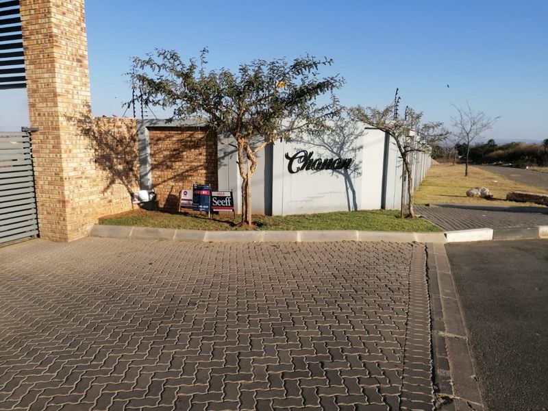 Entrance view of the property featuring a paved driveway, perimeter wall with electric fencing, and brick pillar detailing.