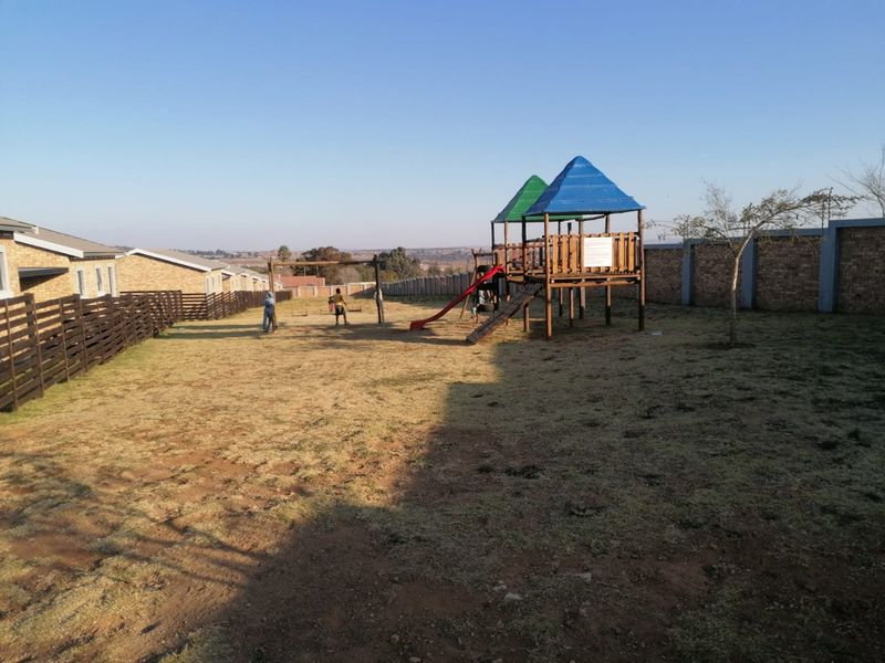 Communal garden area featuring a playground structure, enclosed by brick perimeter walls and wooden fencing.