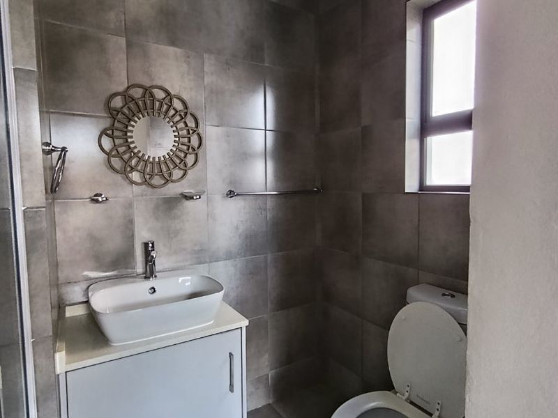 A modern bathroom featuring grey wall and floor tiles, a white vanity cabinet with a vessel sink, and a standard toilet.