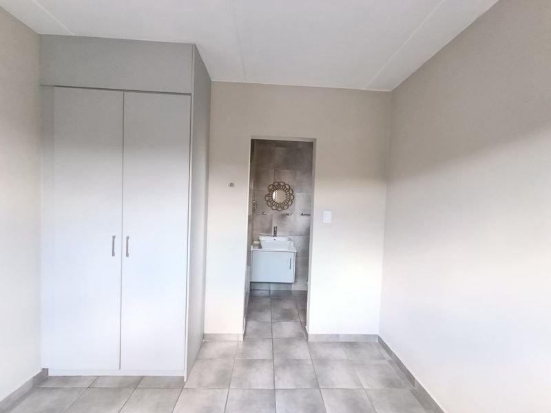 A clean, neutral bedroom featuring tiled flooring, a built-in wardrobe, and direct access to an en-suite bathroom with a vanity basin.
