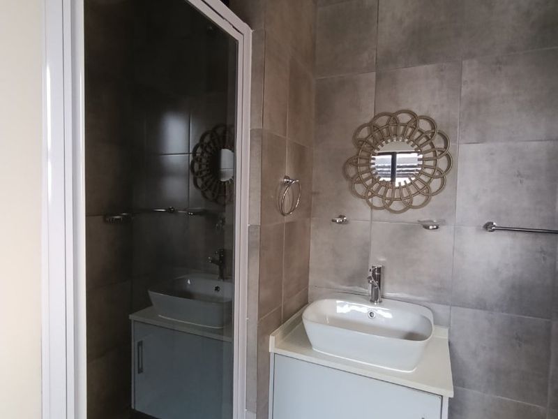 Modern bathroom featuring a glass shower enclosure, a floating vanity cabinet with a vessel sink, and neutral grey wall and floor tiling.