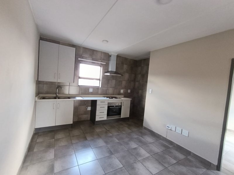A clean, functional kitchen featuring built-in cabinetry, a stainless steel oven and hob, extractor fan, and neutral tiled flooring and backsplash.