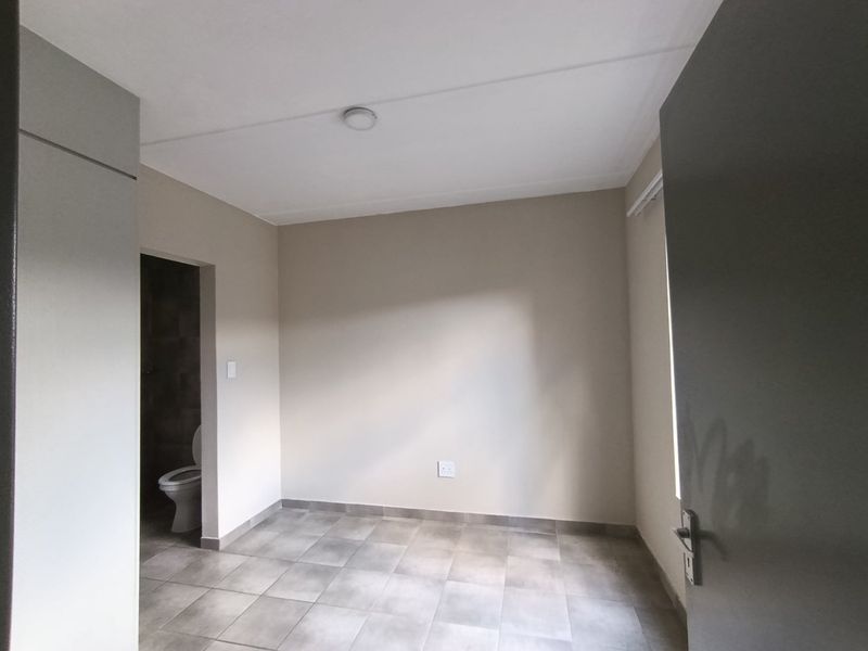 An empty bedroom featuring neutral wall paint, tiled flooring, and an adjacent en-suite bathroom access point.