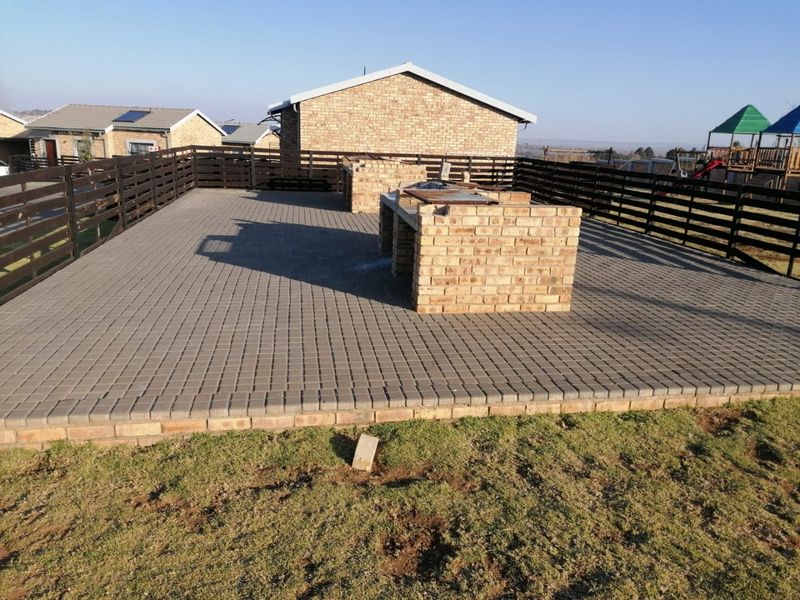 Spacious paved outdoor patio area featuring a built-in brick braai and enclosed by timber perimeter fencing.