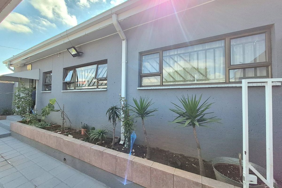 Rear exterior view of the property featuring a tiled planter box, security-fitted aluminium windows, and functional guttering systems.