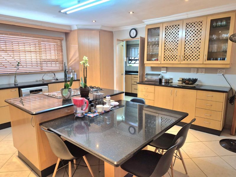 Spacious kitchen featuring light wood cabinetry, dark granite countertops, a central island with integrated seating, and tiled flooring.