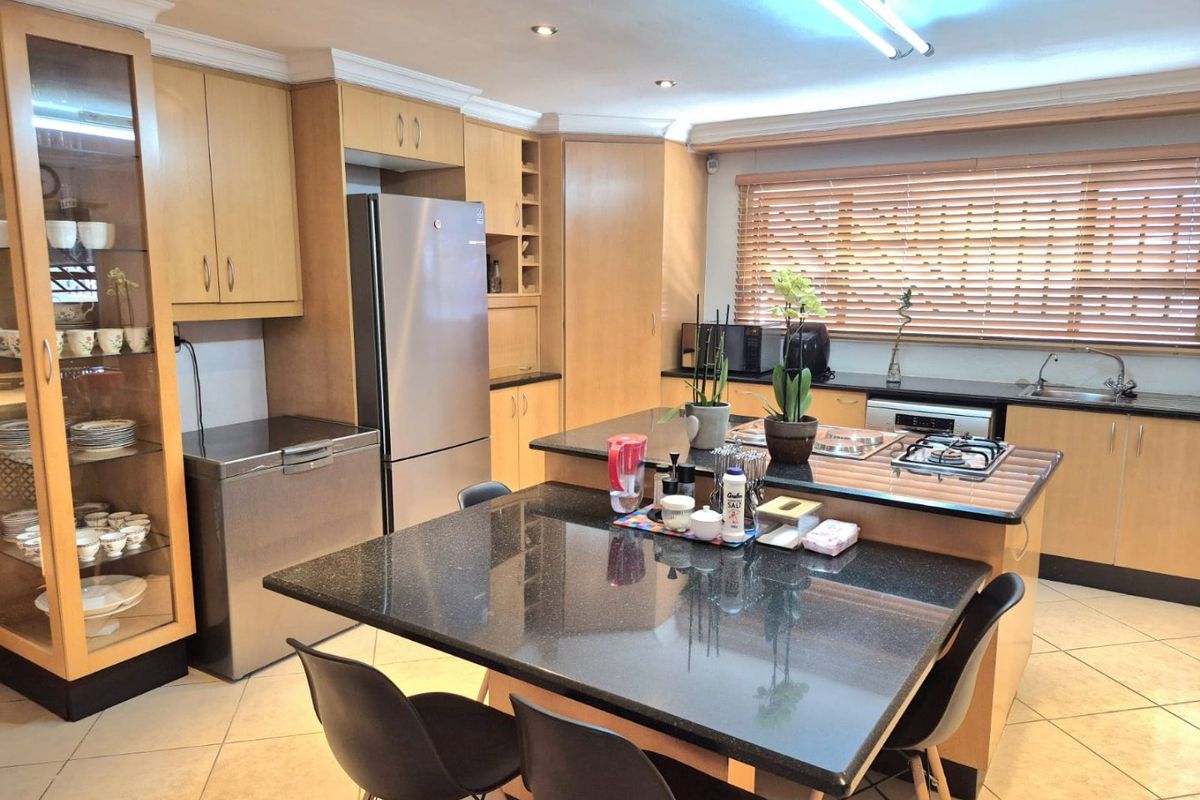 Spacious kitchen featuring light wood cabinetry, dark granite countertops, a central island with seating, and a gas hob, offering a functional and well-lit workspace.