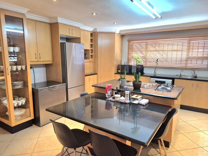Spacious kitchen featuring light wood cabinetry, dark granite countertops, a central island with seating, and a gas hob, offering a functional and well-lit workspace.