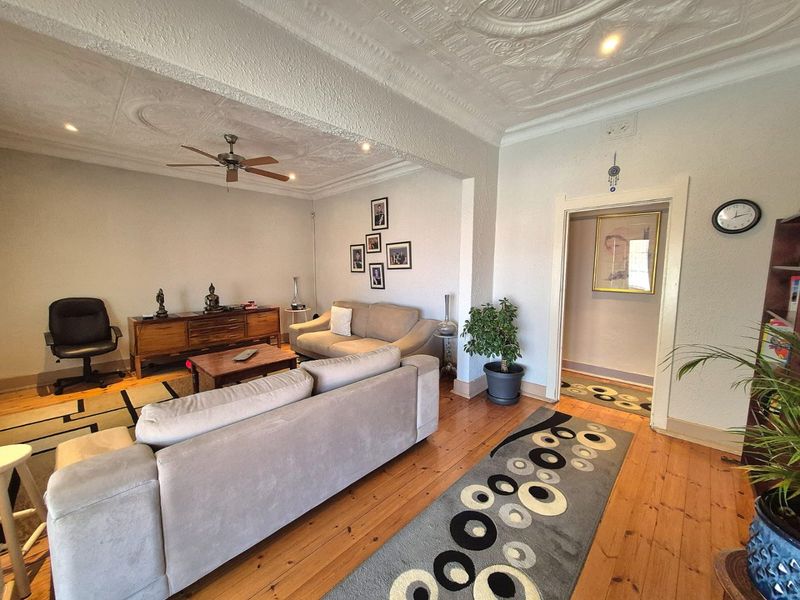 Spacious living room featuring original hardwood flooring, decorative plaster ceilings, and a ceiling fan, providing a comfortable and character-filled living space.