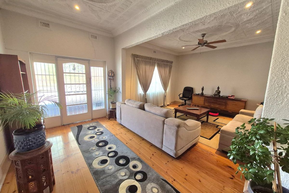 Spacious living area featuring original hardwood flooring and a decorative pressed metal ceiling, providing a classic character feel with integrated ceiling fan and lighting.