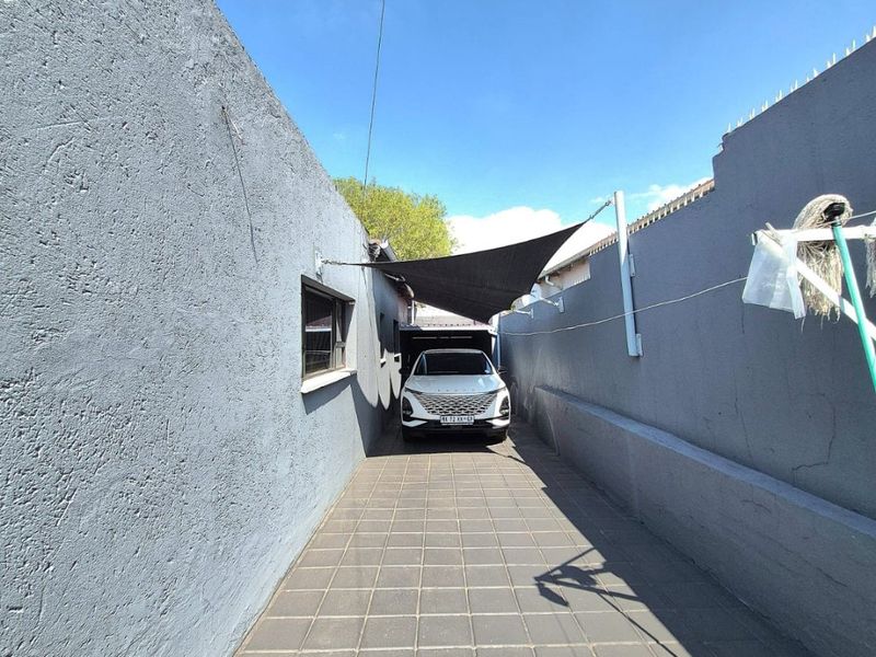A paved side driveway or rear access area featuring high perimeter boundary walls, security spikes, and a shade sail for vehicle protection.