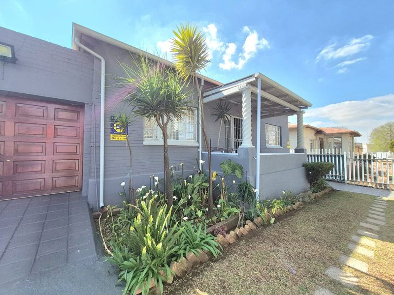 Front elevation of a residential house featuring a garage, covered porch with decorative columns, and a landscaped garden area.