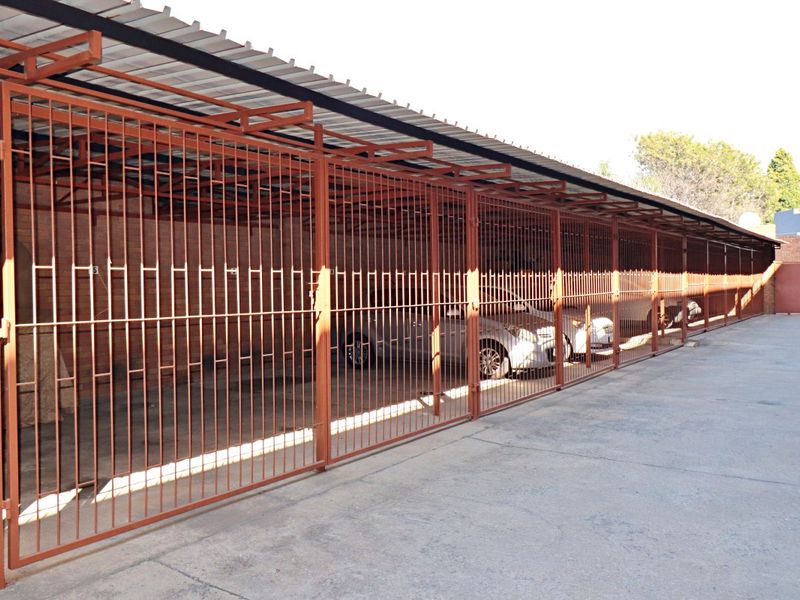 A row of covered parking bays featuring secure metal gate enclosures and a corrugated roof structure.