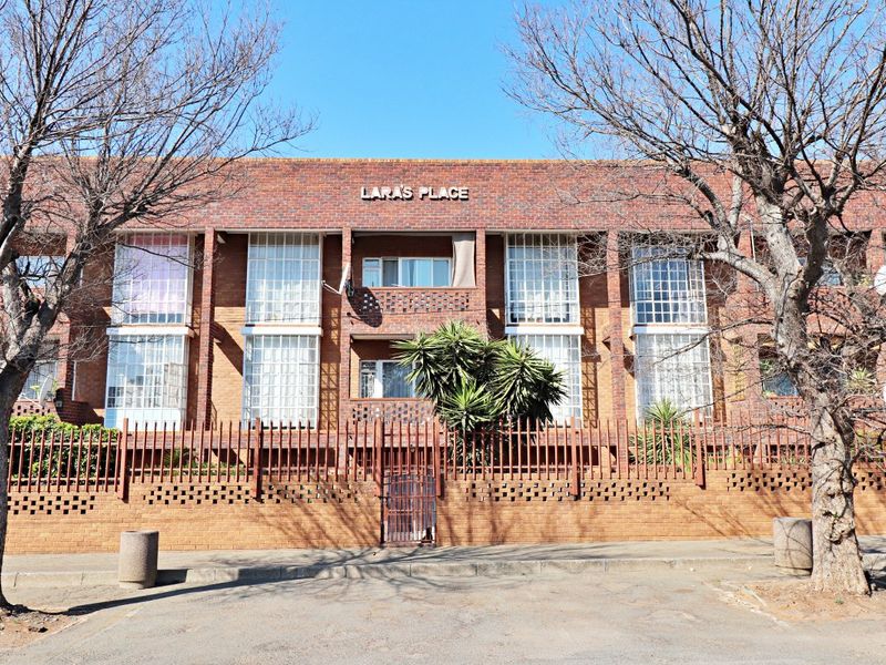Front elevation of Lara's Place apartment complex, featuring a classic brick facade, security fencing, and large glass block window sections.