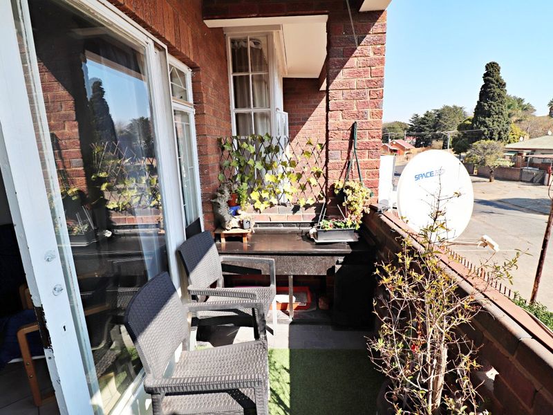 A compact balcony featuring brick wall construction, a sliding glass door entrance, and a metal railing overlooking the street.