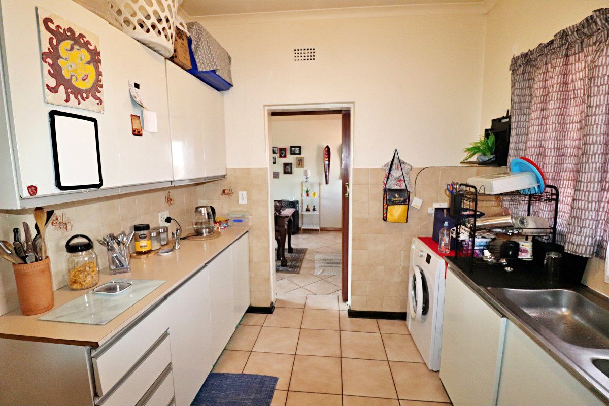 Functional kitchen featuring built-in cabinetry, tiled backsplash, and dedicated plumbing for a washing machine, providing a practical workspace with direct access to adjacent rooms.
