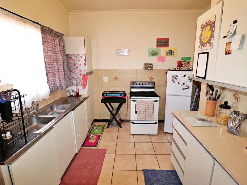 A functional galley-style kitchen featuring tiled flooring, laminate countertops, a double bowl stainless steel sink, and a freestanding oven with tiled splashback.
