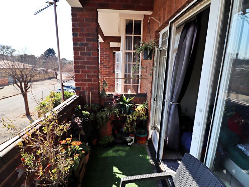 A covered balcony featuring exposed brick walls, a metal railing, and direct access to the interior through a sliding glass door.