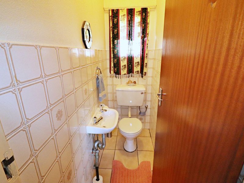 A compact guest bathroom featuring ceramic wall and floor tiles, a wall-mounted basin, and a standard toilet.