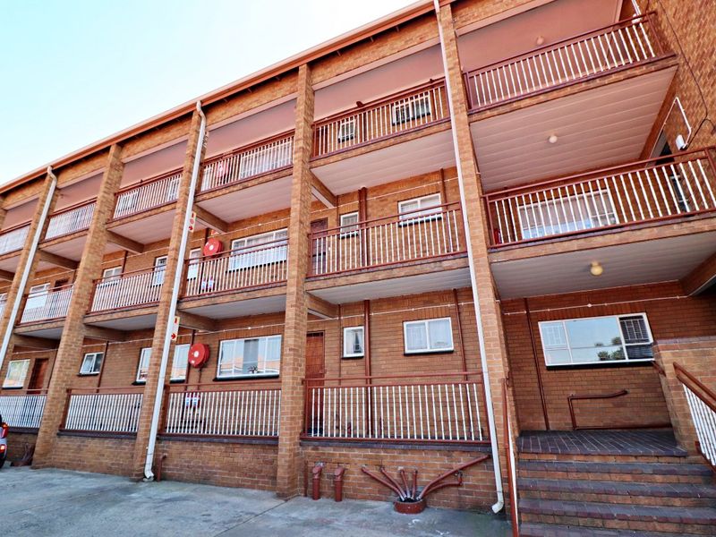 Multi-story apartment building exterior featuring face brick construction, private balconies with metal railings, and an external staircase.