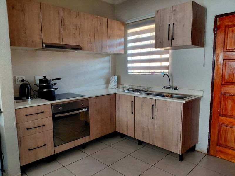Functional kitchen featuring wood-look laminate cabinetry, built-in oven, electric hob, extractor fan, and stainless steel sink with tiled flooring.