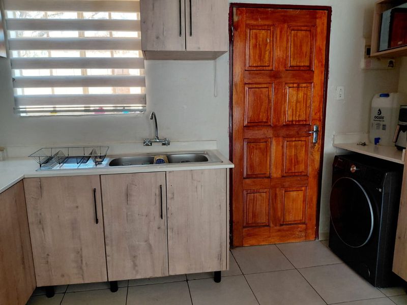 A functional kitchen area featuring light wood-look cabinetry, a double bowl sink, tiled flooring, and a solid wood door.