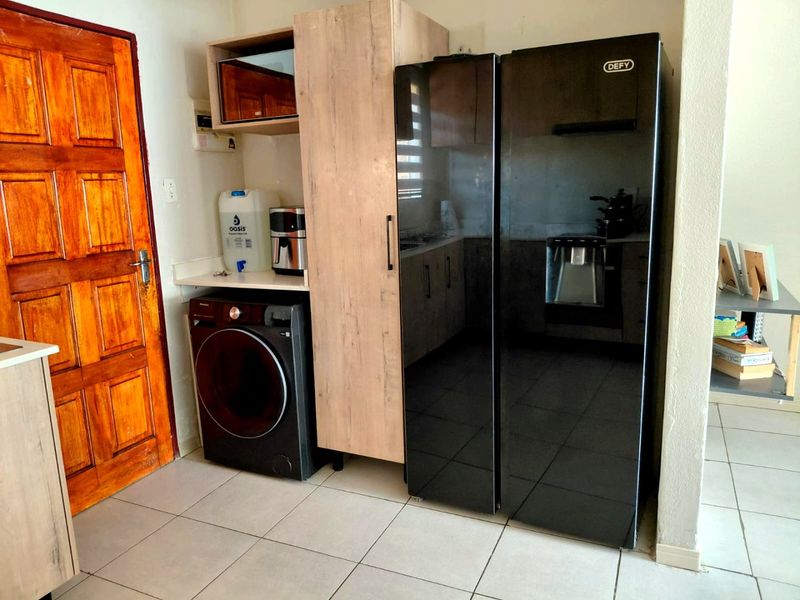 A functional kitchen area featuring built-in cabinetry, tiled flooring, and space for integrated appliances, adjacent to a solid timber door.