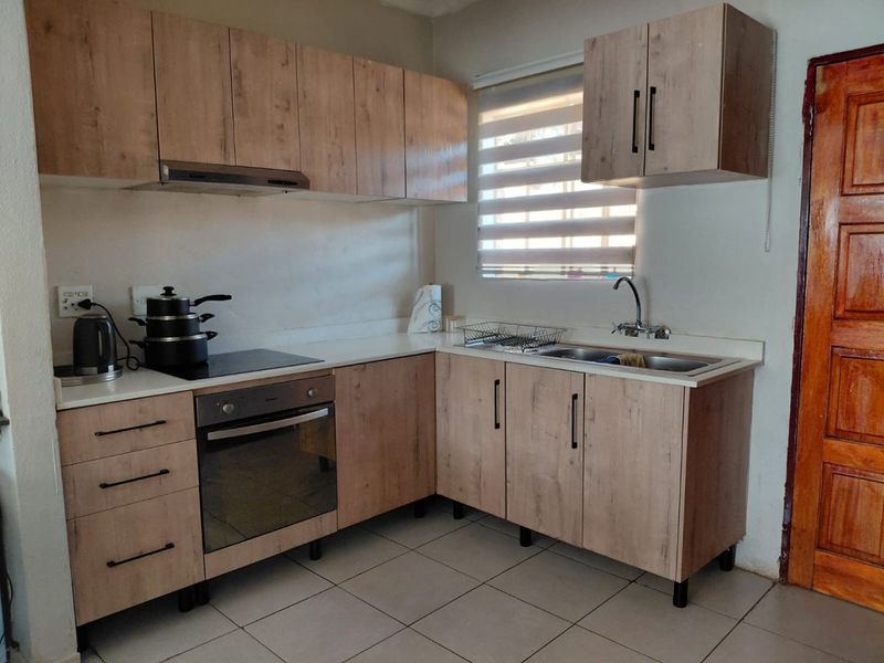 Functional kitchen featuring light wood-look cabinetry, built-in oven, electric hob, and tiled flooring with a window providing natural light.