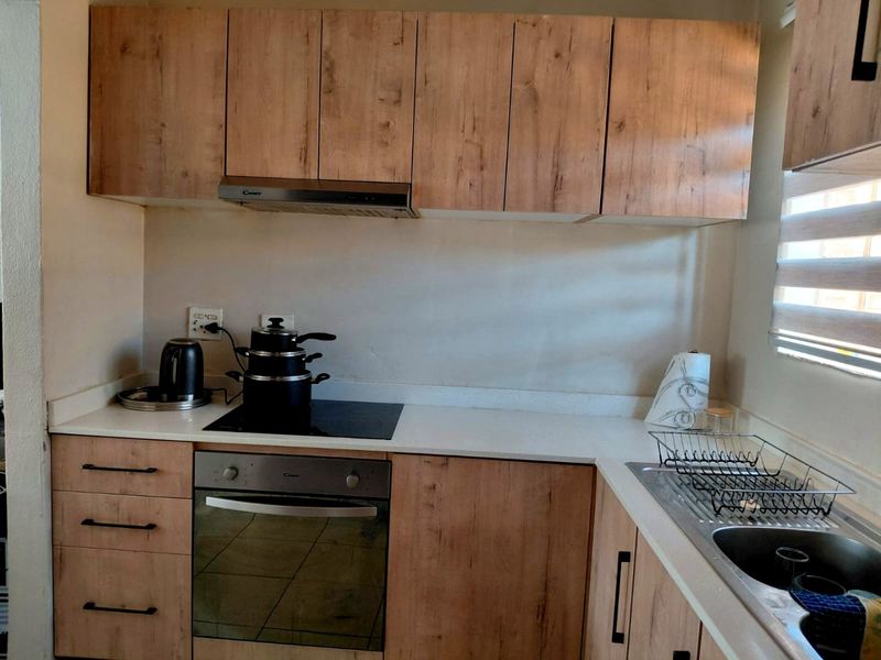A functional kitchen featuring wood-look cabinetry, stone countertops, a built-in oven, electric hob, and a stainless steel sink.