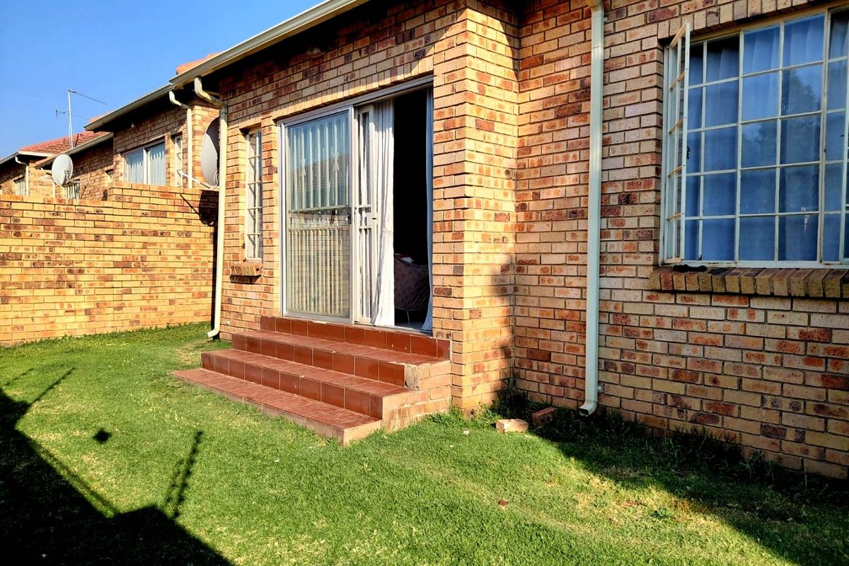 Rear view of a face brick house featuring a sliding door entrance with tiled steps and a small private garden area.