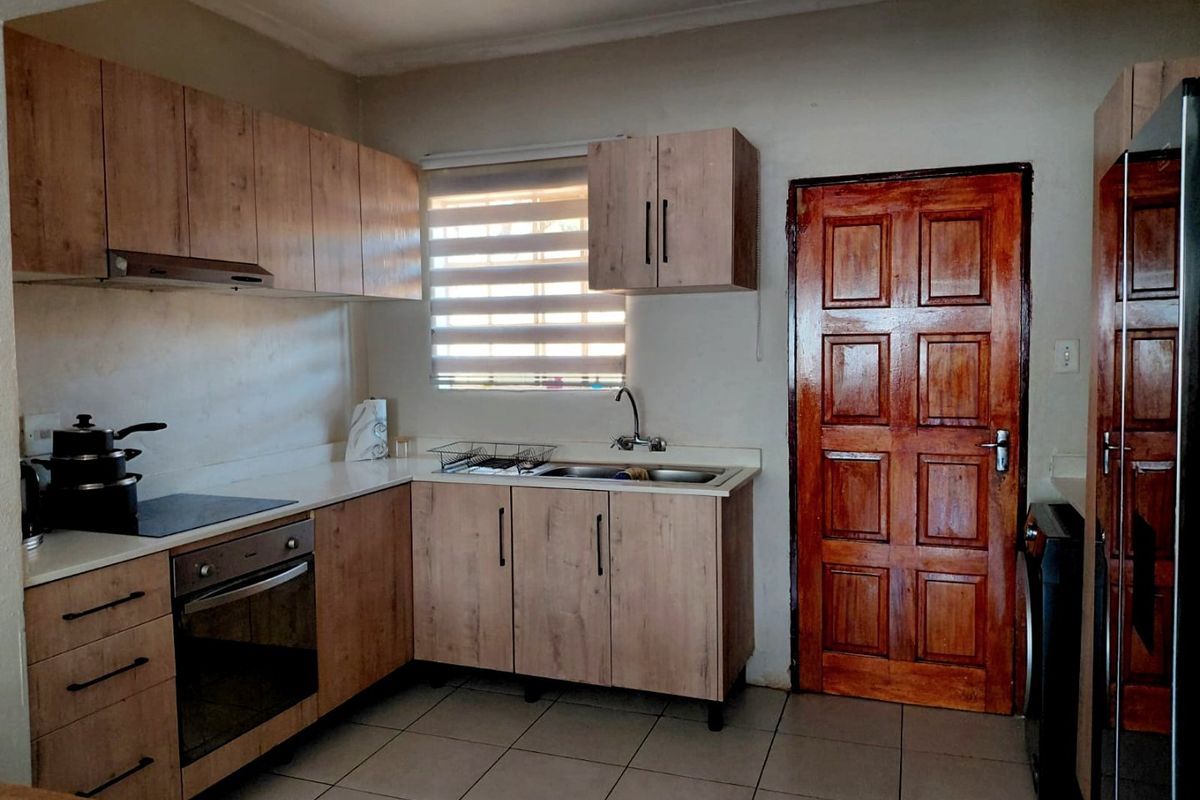 A functional kitchen featuring light wood-look cabinetry, laminate countertops, built-in oven and hob, and tiled flooring with a window providing natural light.