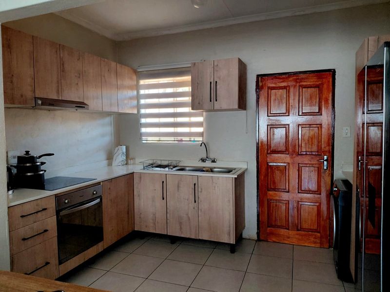 A functional kitchen featuring light wood-look cabinetry, laminate countertops, built-in oven and hob, and tiled flooring with a window providing natural light.