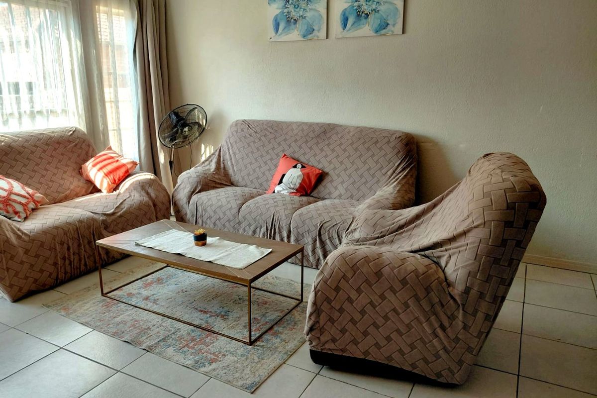 A living room area featuring neutral tiled flooring and large windows with curtain tracks, providing a functional and well-lit space.