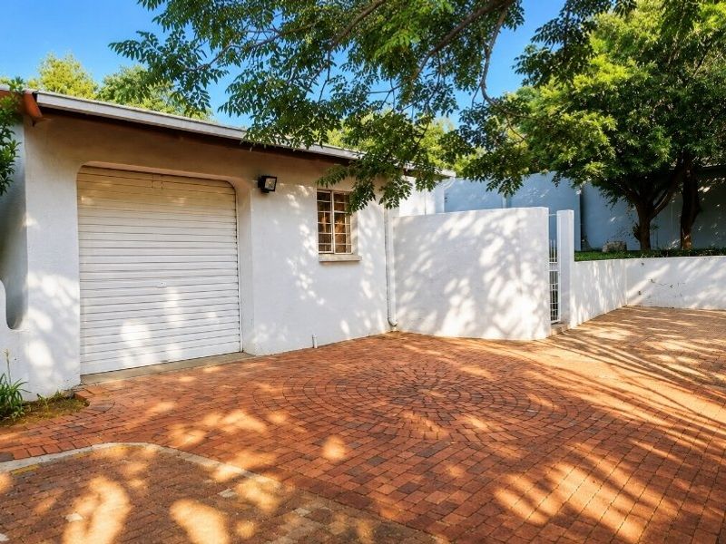 A well-maintained single garage featuring a white roller shutter door and a spacious brick-paved driveway area.