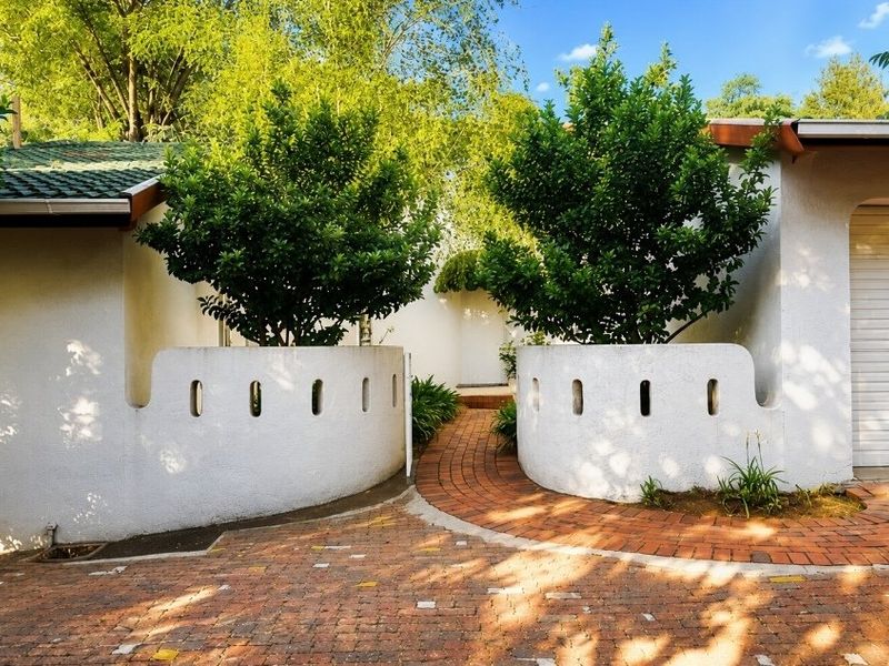 Front entrance view featuring a brick paved driveway and walkway leading to a home with curved masonry boundary walls and a tiled roof.