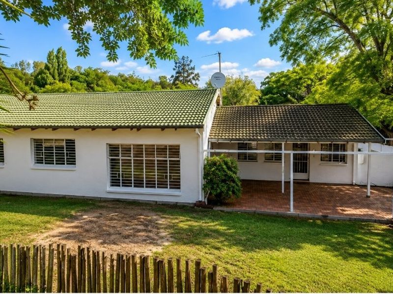 Rear view of the house featuring a tiled roof, a covered brick patio area, and a spacious garden with a wooden fence.