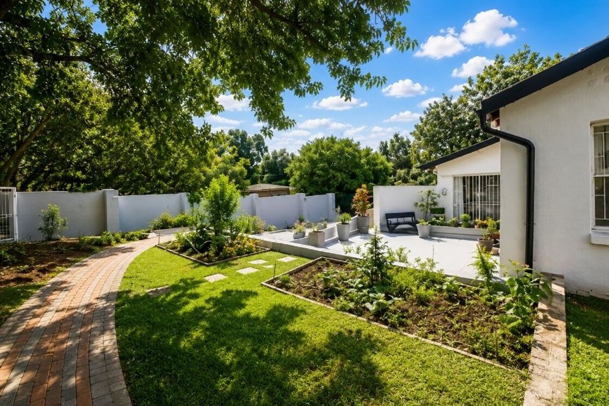 A well-maintained rear garden featuring a brick paved pathway, raised garden beds, and a concrete patio area adjacent to the main dwelling.