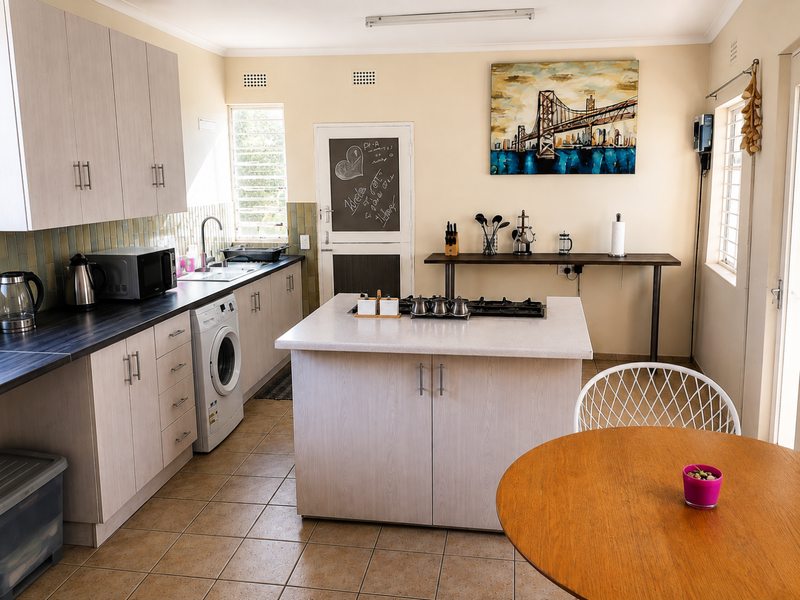 A functional kitchen featuring light wood-finish cabinetry, a central island with a built-in gas hob, tiled flooring, and ample counter space.
