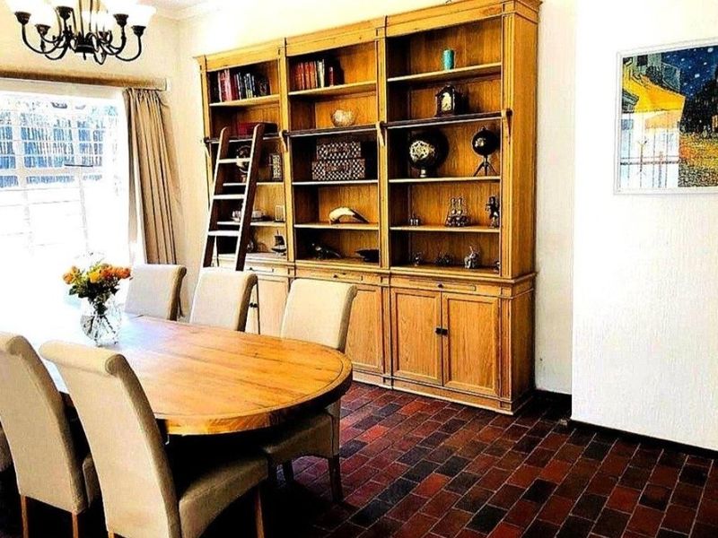 A dining room featuring a large built-in wooden shelving unit with a library ladder and traditional terracotta brick flooring.