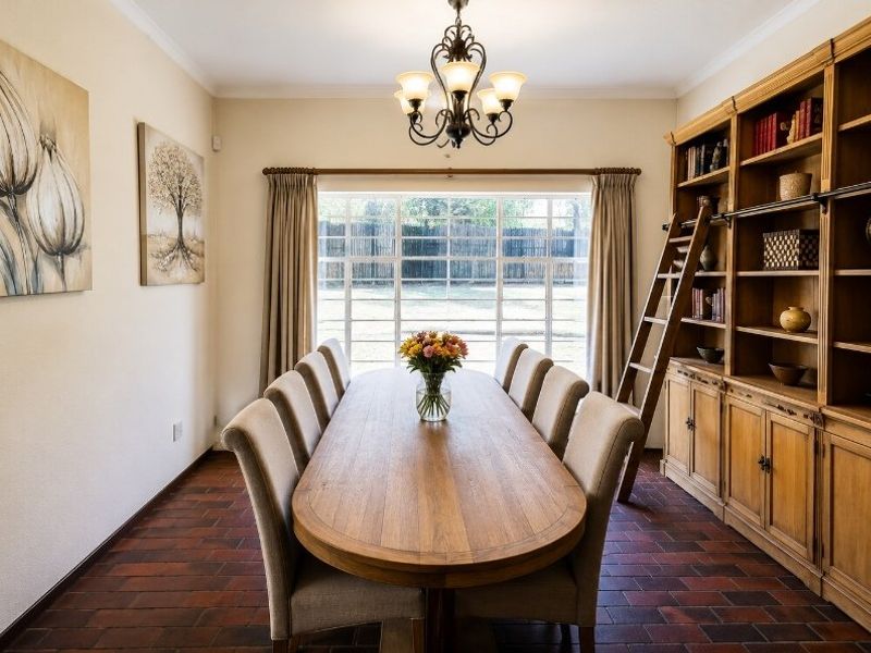 A formal dining room featuring classic brick flooring, a large window with garden views, and a substantial built-in wooden library shelving unit with ladder.
