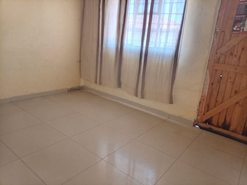 An empty bedroom featuring tiled flooring, a wooden door, and a window fitted with security bars.