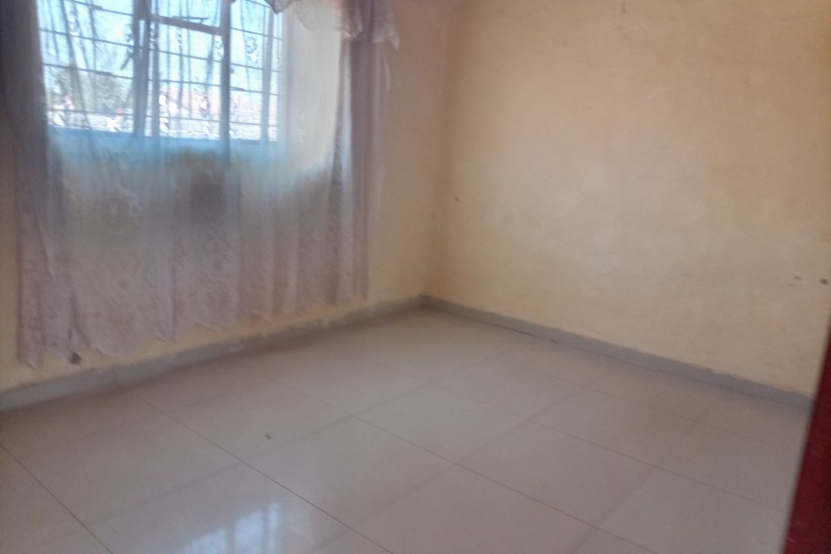 A vacant bedroom featuring tiled flooring and a window fitted with security bars, offering a blank canvas for potential interior updates.
