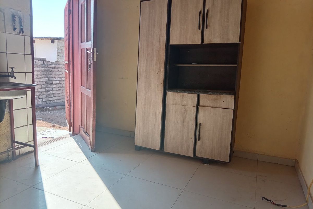 A basic kitchen area featuring tiled flooring, a sink, and a standalone storage unit, with direct access to the exterior.